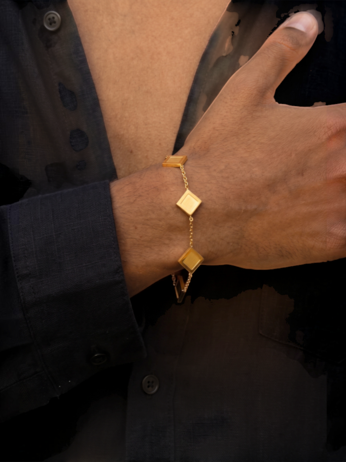 LOUVOND The Prisma Link Bracelet met vijf gouden klaverbedels gedragen om de pols tegen een zwart overhemd.