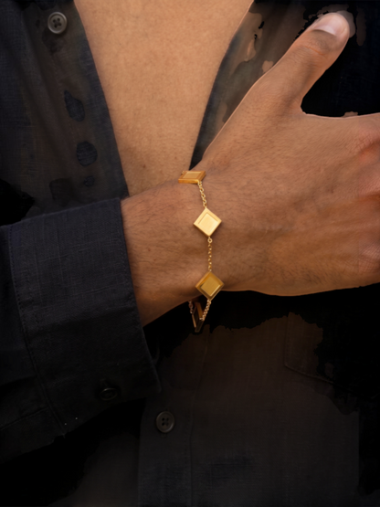 LOUVOND The Prisma Link Bracelet met vijf gouden klaverbedels gedragen om de pols tegen een zwart overhemd.