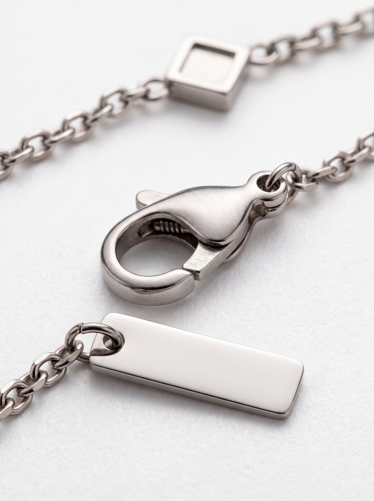 LOUVOND Rhombus Link armband met zilverkleurige schakelketting, karabijnsluiting en rechthoekig merkplaatje.